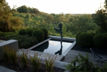 The setting sun on the distant forested hills form a dramatic backdrop for the reflecting pool; and the fluid lines of the sculpture, “Day” by Gary Weisman.