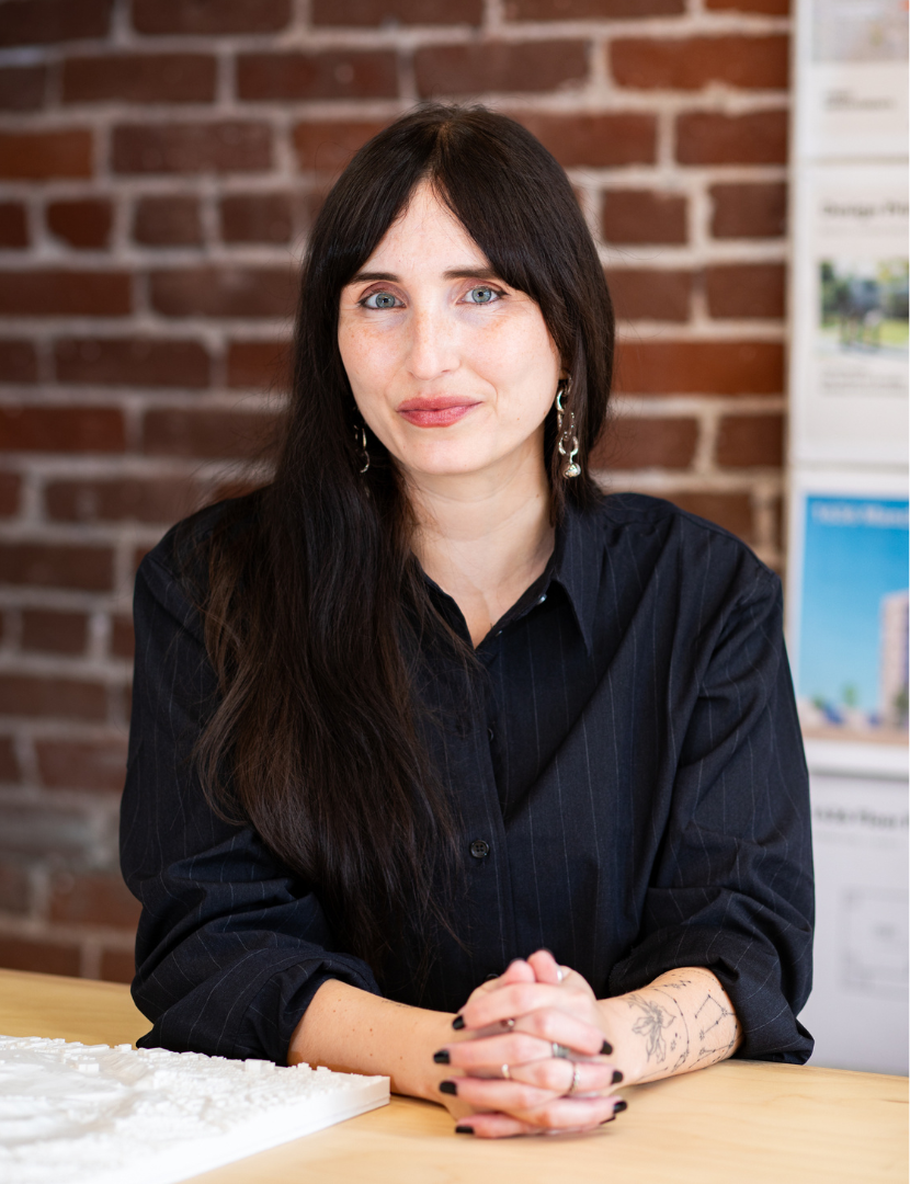 Alexa Vaughn sitting with hands clasped at a table, with long dark hair worn down and wearing a buttoned collared shirt.